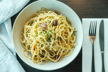 Traditional italian spagnetti pasta with olives, anchovies and sardines, parsley on a wooden table with napkin and cutlery
