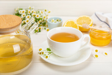 Chamomile tea in a white cup on a white texture background. Natural hour with chamomile flowers. Herbal tea. Immunity tea.Natural healer concept. Healthy detox drink.Close up. Place for text. 