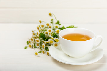 Chamomile tea in a white cup on a white texture background. Natural hour with chamomile flowers. Herbal tea. Immunity tea.Natural healer concept. Healthy detox drink.Close up. Place for text. 