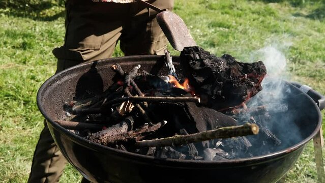 Round grill with burning wood. An unrecognizable person stirs the coals. Preparing for a barbecue.