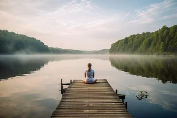  Woman sitting on a wooden pier on a lake in the misty morning. Generative AI © mila103