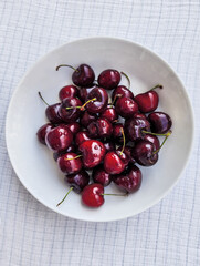Ripe cherries with water drop on a white plate. Summer berries on a light background.