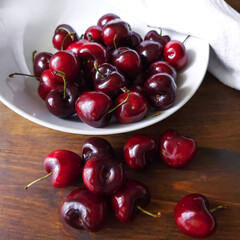 Cherry fruits. Dark red berries in a white plate and scattered on a wooden table.
