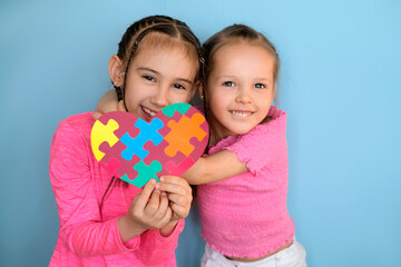 Two happy cheerful sisters show the symbol of autism with the image of colored puzzles