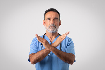 Serious caucasian senior doctor surgeon in blue uniform crossed arms, making stop sign
