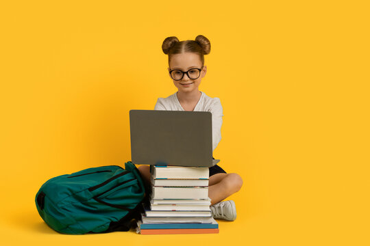 Online Learning. Little Girl Doing Homework On Laptop, Sitting At Book Stack