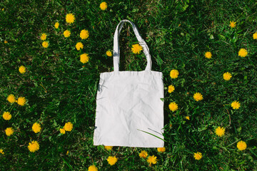 White cotton or mesh bag on dandelion green grass background. Zero waste, no plastic eco friendly shopping, recycling concept. Blank mockup shopper with place for artwork or text. Flat lay, copy space
