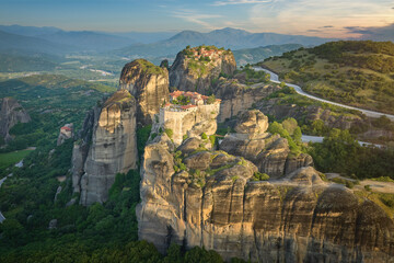 Fototapeta na wymiar Aerial view of Meteora Monastery complex on rocks, illuminated by rising sun against mountains in background. UNESCO World Heritage Site. Greece.