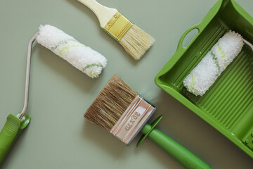 Wall paint roller and brush on green background, top view
