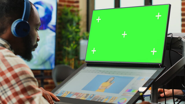 Male employee working with greenscreen and retouching software, looking at isolated mockup template on computer. Young artist using chroma key display with copyspace and editing interface.