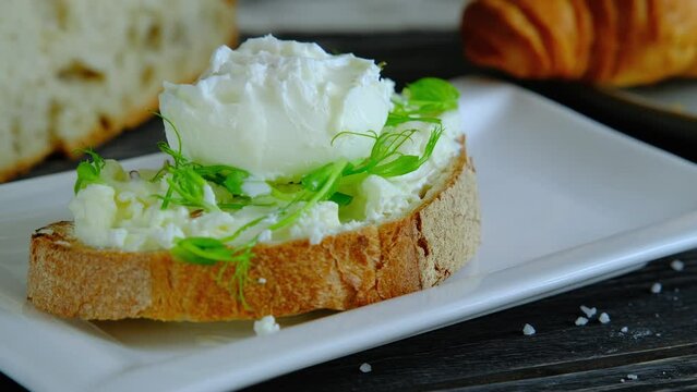 Pouring sauce on benedict egg with stracciatella cheese and bread crust. healthy breakfast, poached egg on toast, slow motion video, 4k high quality footage