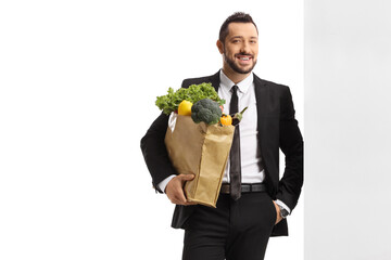 Businessman with a grocery bag leaning on a wall