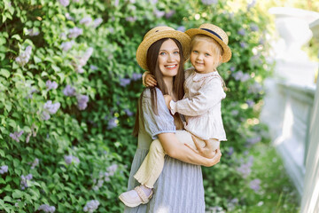 A mother lovingly hugs and kisses her daughter at sunset in a park of sunflowers. Happy family. Unity with nature. Mother's Day. Children's Day. Tender portrait of mother and baby