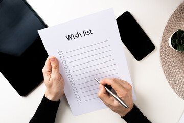 man fills the wish list. male hands hold a pen and make notes. laptop, phone, coffee on the table