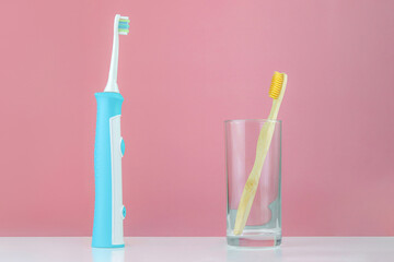 Bamboo toothbrush in a glass cup and opposite an electric toothbrush