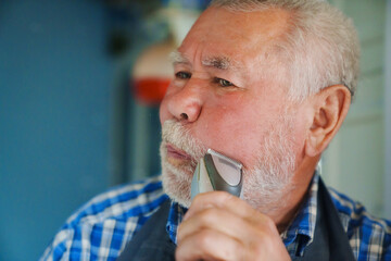 An elderly man trims his beard with an eclectic razor. ease of use of clippers.