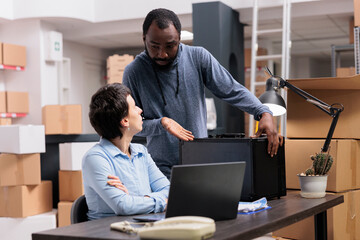 Fototapeta premium Workers discussing about metallic box while checking transportation logistics for package delivery on laptop computer. Storehouse manager analyzing online shipping order working in warehouse
