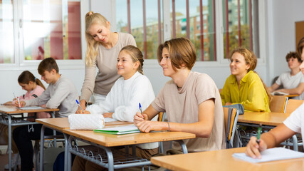 Pupils write in notebooks while sitting at desks in a school class
