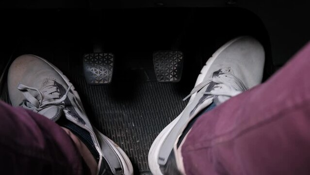 Men's feet in sneakers press the clutch, gas, brake. Driving a car with a manual transmission.