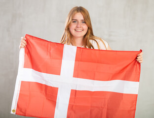 Mirthful girl in arms raised above head holds canvas of national flag of Denmark. concept of unity and self-determination. Gray background