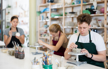 Young man in apron modeling clay pottery in workshop
