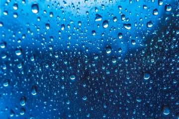 Naklejka na ściany i meble Water drops condensed on a glass window, rainy weather, raindrops, bluish background. Generative AI