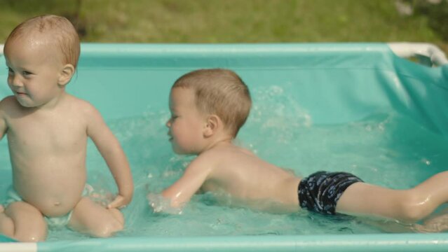 two happy laughing kids swim splash water blue pool outdoors backyard summer day. children brothers have fun water garden. rubber inflatable swimming pool outside. male siblings boys dive swim pool 