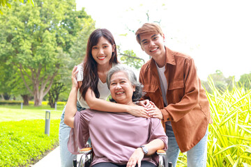 Family concept. Daughter and son bring elderly mother in wheelchair to breathe fresh air at outdoor...