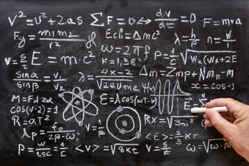 Mano humana señalando operaciones y formulas de física cuántica escritas con una tiza en la...