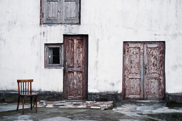 Fototapeta na wymiar White wall facade of an old Georgian house with wooden closed doors, windows and a lone wooden chair.