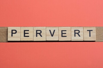 text the word pervert from gray wooden small letters with black font on an red table
