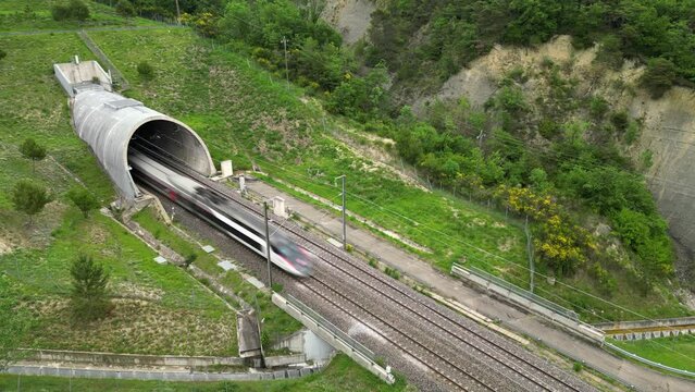 Panoramic drone view of a high-speed passenger train entering a tunnel at the foot of the mountain. Overlooking the surrounding mountains in southern France