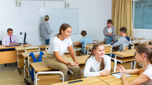 Teenagers Students Of Middle School Chatting On Break Sitting At Desks