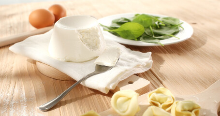 ricotta cheese with spinach and raw tortelloni. traditional italian cheese on a white napkin. ingredients for tortellini pasta. visual recipe. sunny day. angle view.
