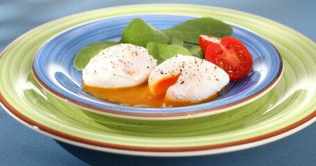 poached eggs with vegetables on a plate. traditional breakfast. colored background. sunny day. angle view. 