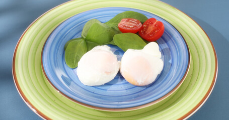 poached eggs with vegetables on a plate. traditional breakfast. colored background. sunny day. angle view. 