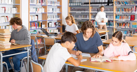 Group of schoolchildren reading books together in library and preparing for the school exam