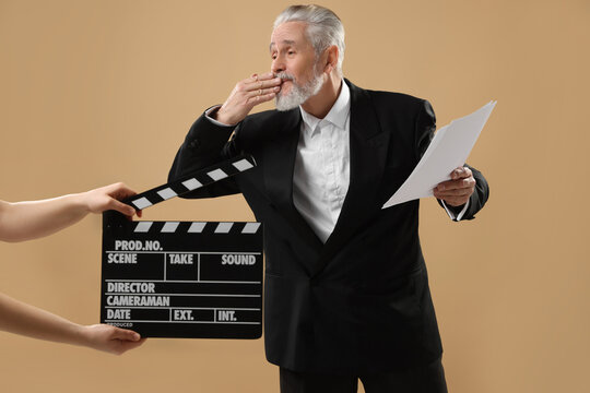 Senior actor performing role while second assistant camera holding clapperboard on beige background. Film industry