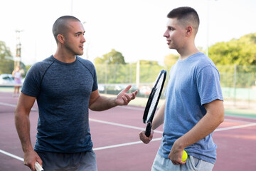 Two men with rackets in their hands chatting after playing padel on the tennis court outdoor
