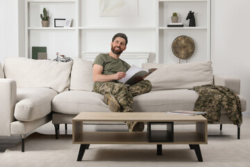 Happy soldier reading magazine on sofa in living room. Military service