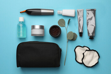 Preparation for spa. Compact toiletry bag and different cosmetic products on light blue background, flat lay