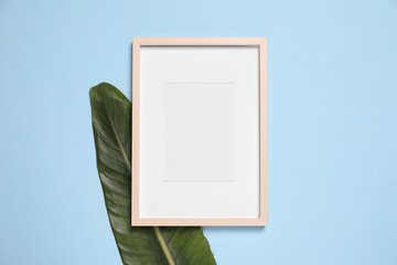 Empty photo frame and green leaf on light blue background, flat lay. Space for design