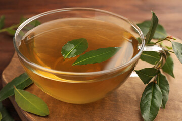 Cup of freshly brewed tea with bay leaves on wooden table, closeup