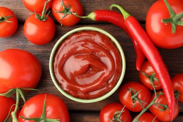 Bowl of tasty ketchup, chili peppers and tomatoes on wooden table, flat lay