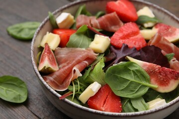 Tasty salad with brie cheese, prosciutto, strawberries and figs on table, closeup