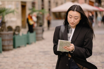 Portrait young happy asian woman tourist in casual clothes on old city street in europe while checking direction on map and navigation on smartphone