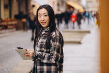 Portrait of a beautiful brunette Korean woman holding a map and comparing it with smartphone navigation on the streets of the old city. Asian tourist woman traveling in Europe.