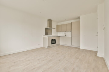 an empty living room with white walls and wood flooring, the kitchen is in the middle part of the photo