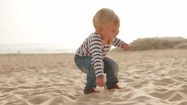 Little blonde boy and smiling mother play on beach