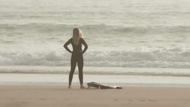 Blonde woman brings surfboard at beach and warm up